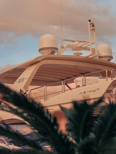 Close-up view of the upper deck of a white Azimut yacht, featuring satellite domes and railings, partially obscured by out-of-focus foliage—a glimpse into the world of luxury services at sea.