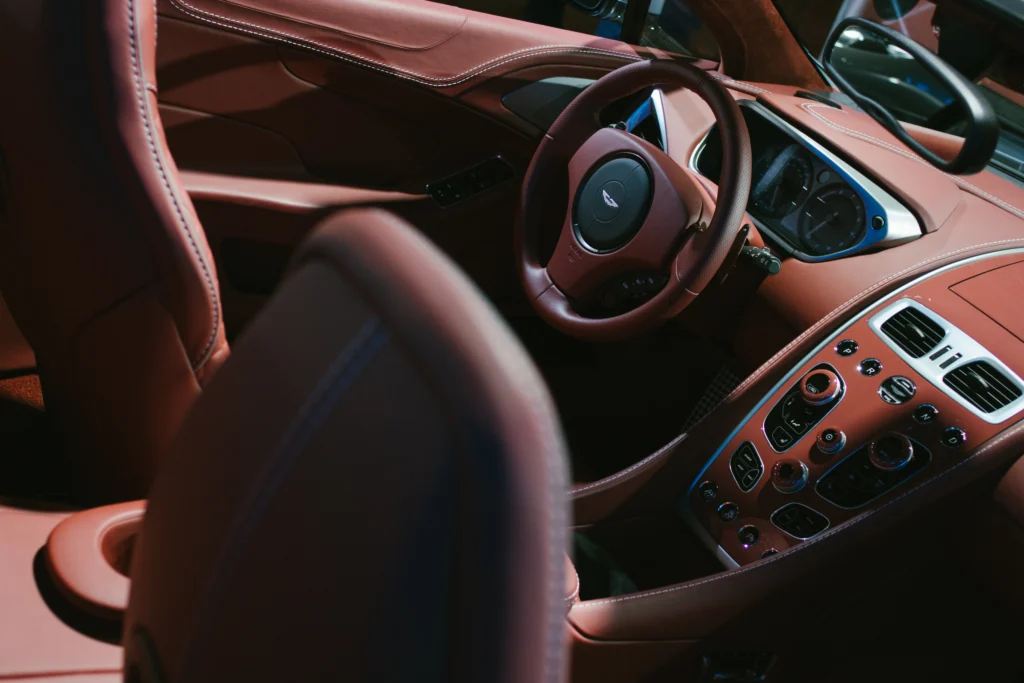 Close-up of a luxury car interior with brown leather seats, steering wheel, and dashboard featuring multiple control buttons and dials.