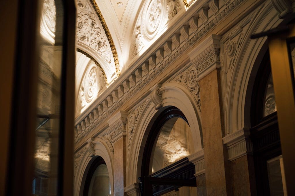 Ornate interior architecture featuring arched doorways, decorative mouldings, and detailed carvings with soft, warm lighting.